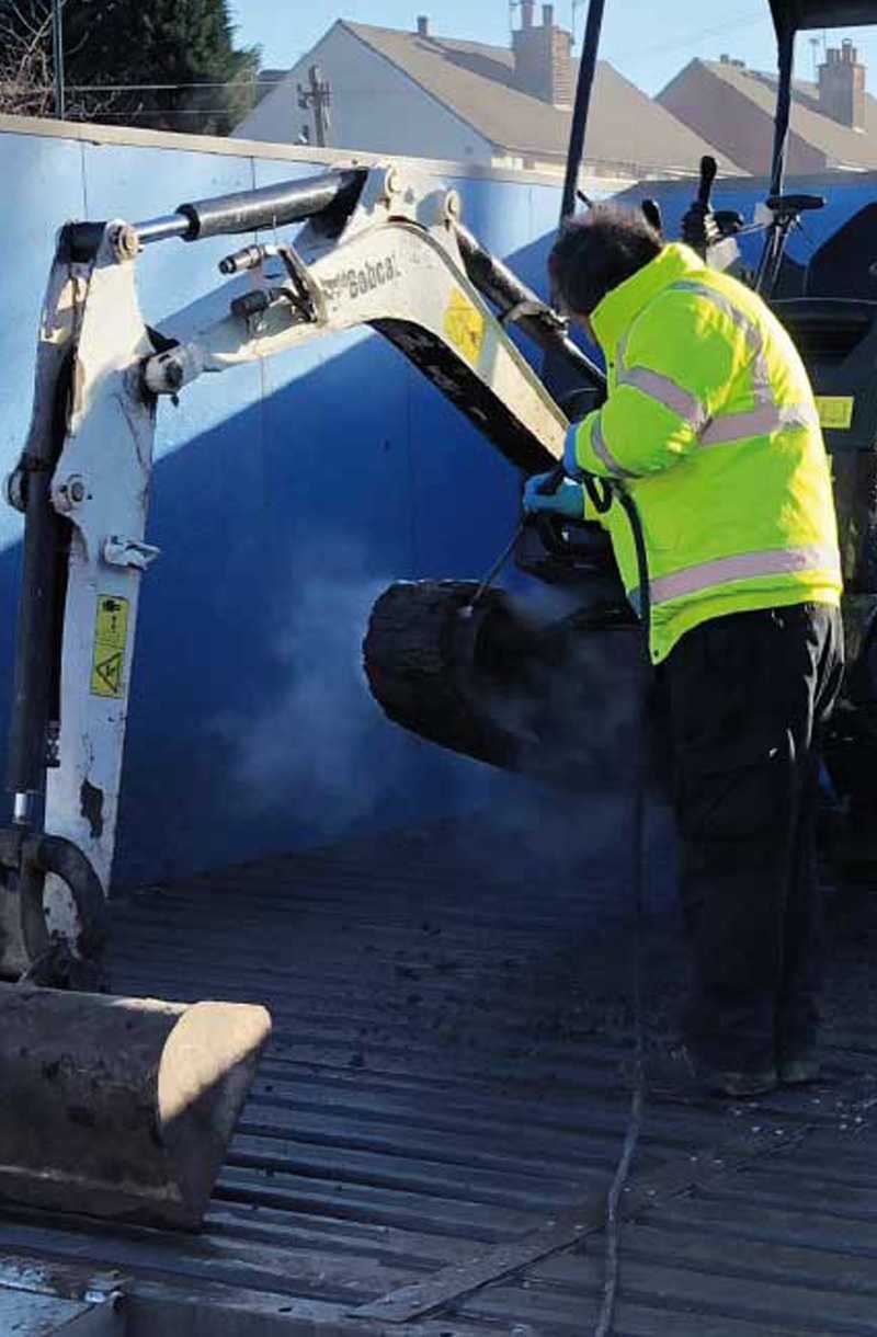 an operator inside a washbay cleaning a working machine in a construction site
