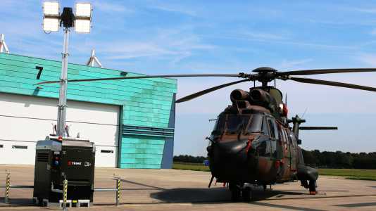 a Trime X-Box standing near a military helicopter during military operations
